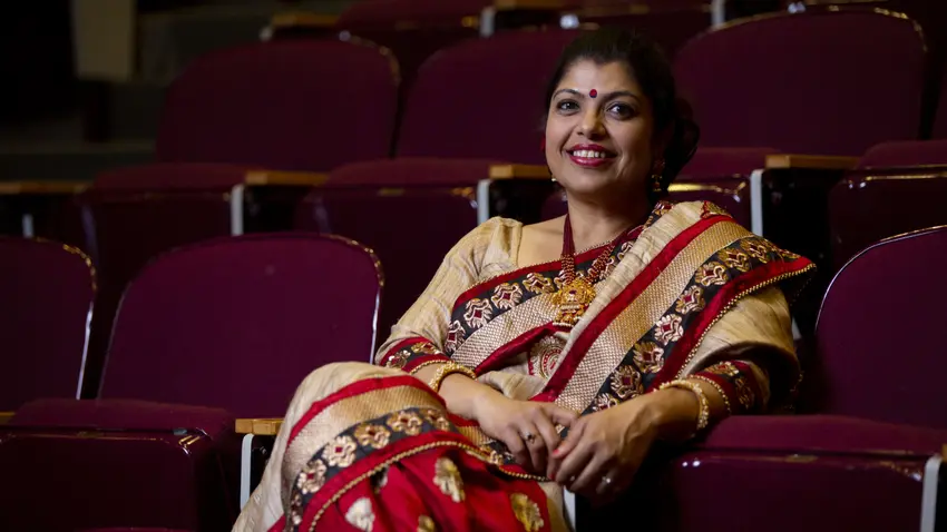 Professor Mita Das, wearing a red and gold embroidered sari, sits in a seat in Wilder Auditorium.