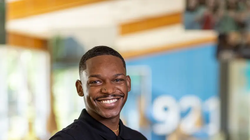 Tyler-Gary Louis leaning on elbow and smiling wearing navy blue polo shirt and light color khaki pants