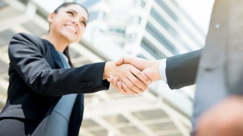 Person wearing a suit shaking a hand in front of a building