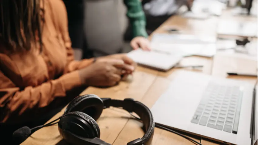 employee working at desk with laptop and headphones nearby