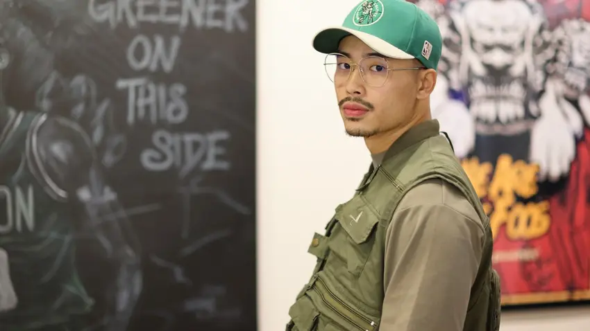 Bentley alumnus Jonathan Yu stands in front of two of his artworks on display in the Bentley Library's RSM Art Gallery
