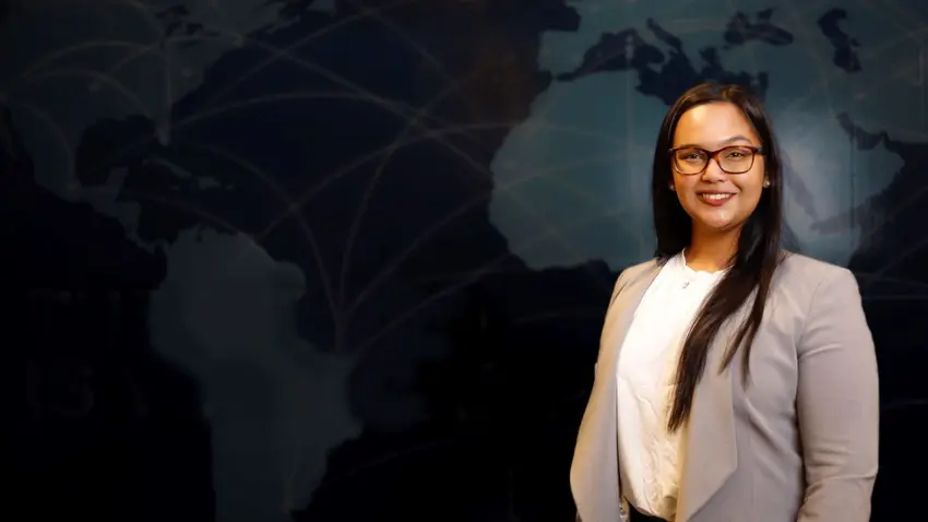Kerisse Seepersad standing in front of wall map wearing white shirt and tan blazer