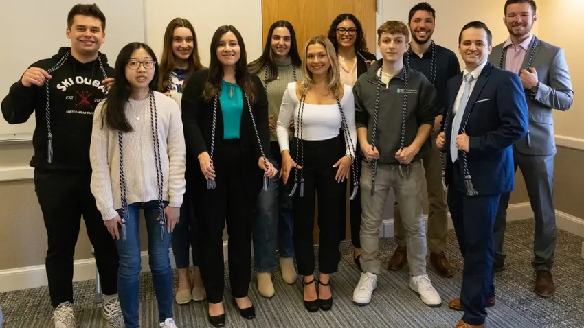 Group photo of 11 members of Bentley's Class of 2023 who were inducted into the inaugural class of Tri-Alpha. All wear tasseled cords in blue and gray —the honor society's colors — that they will wear on graduation day to denote their membership. 
