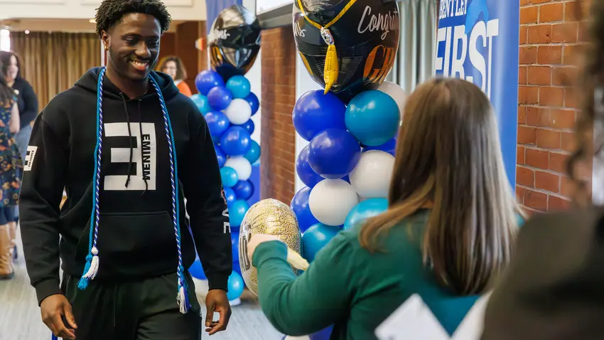 First-Gen Student walking across a stage to receive a cord for graduation
