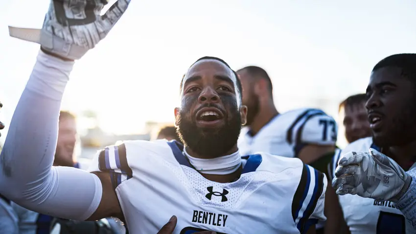 Jailen Branch In white Bentley football uniform with hand in the air