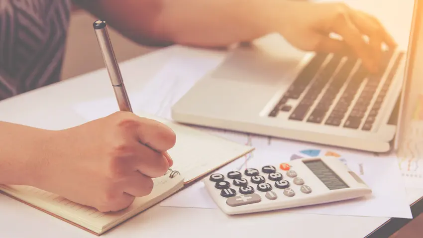 man writing with laptop open and calculator out