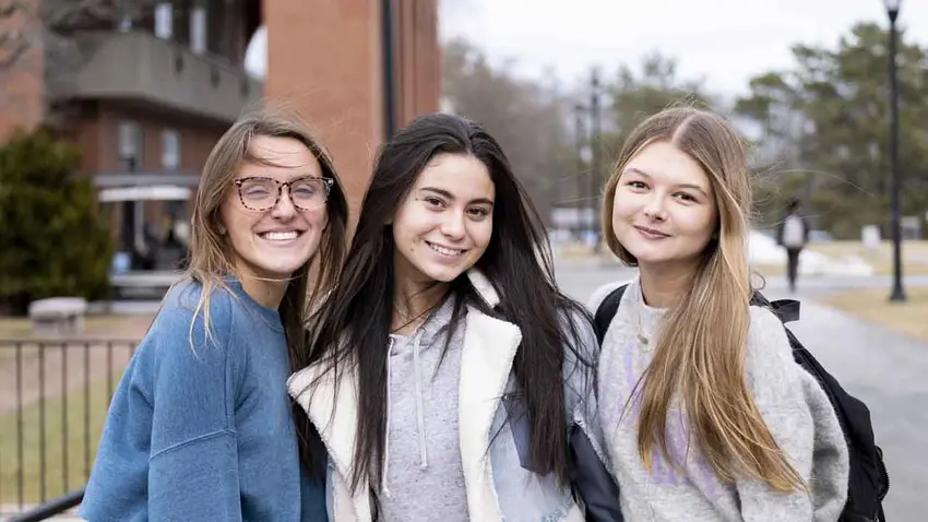 three female students smile on campus