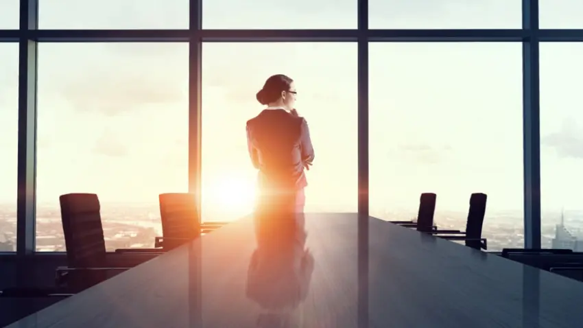 Woman alone in a highrise corporate boardroom looks out over a city scape.ty