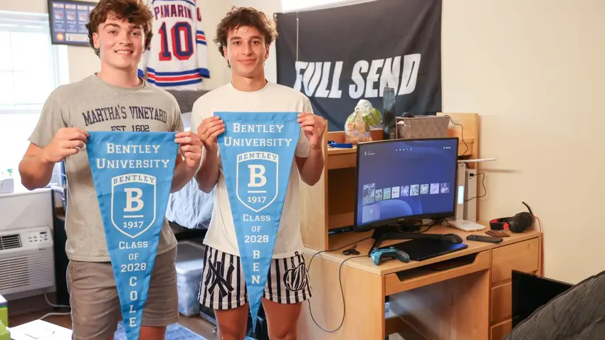 Two Class of 2028 Bentley students holding pennants as they move into their dorm room