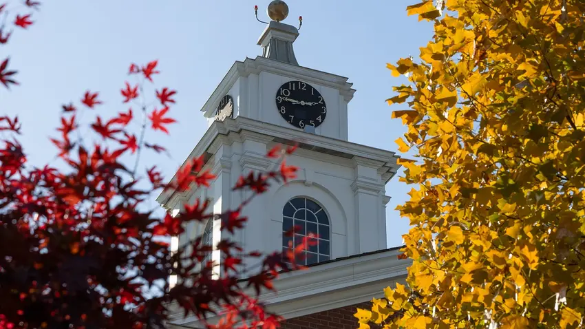 Photo of library's clock tower in background, with russet and amber fall foliage in foreground.in yellow