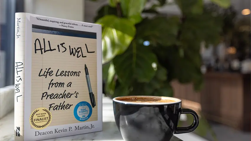 the book All is Well next to a cup of coffee