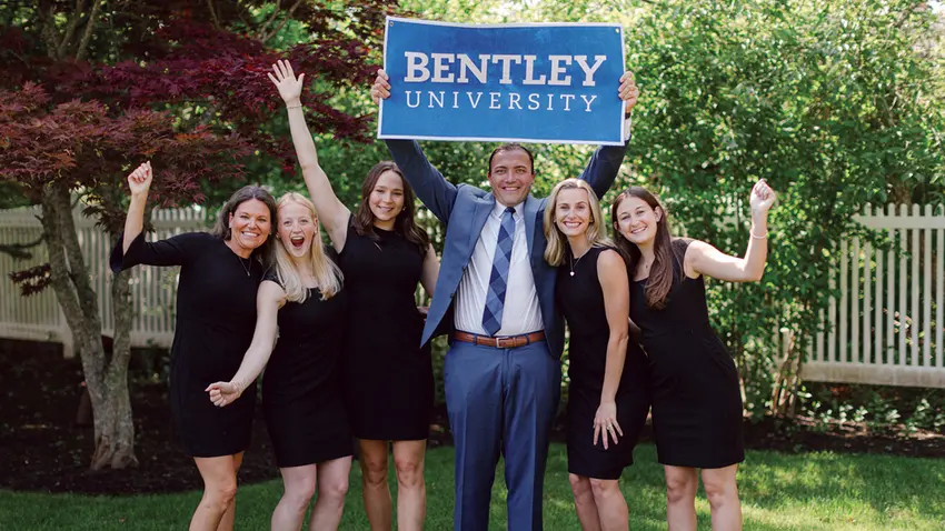 a group of alumni holding up a Bentley University banner