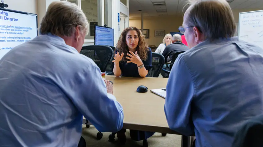 A woman in a dark blue shirt talks to two older men in button downs
