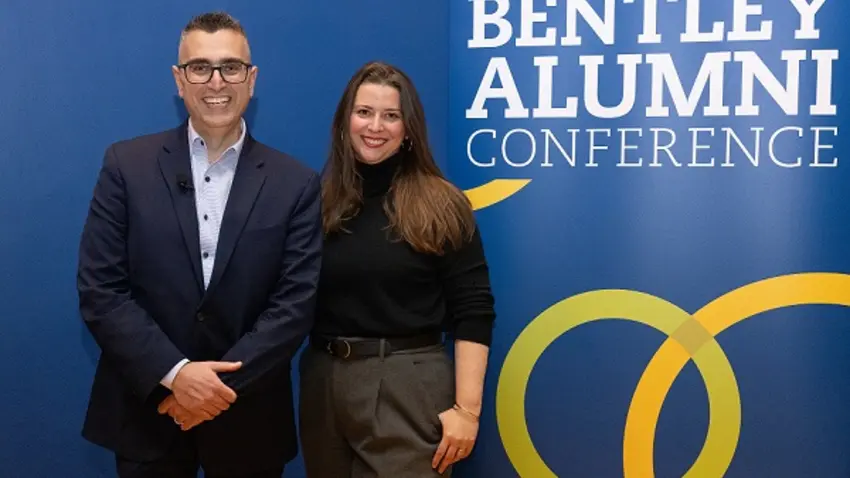 A man and woman pose next to a banner that reads "Bentley Alumni Conference."