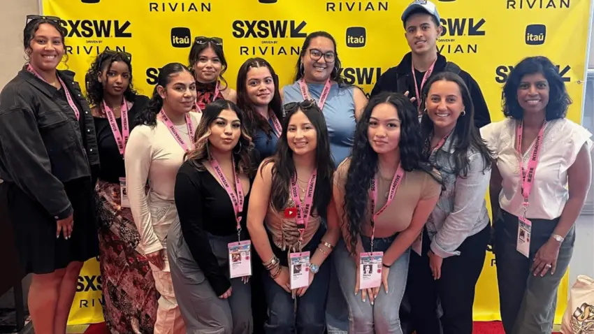 Eleven first generation students pose with Bentley staff member Neelangi Gunasakera in front of a yellow step-and-repeat banner during the 2025 SXSW conference.
