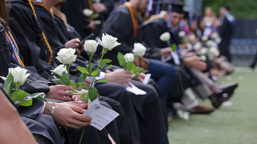 Students wearing caps and gowns hold white roses in honor of classmate who passed away