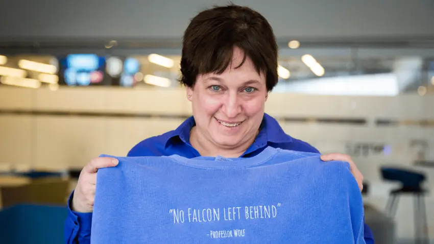 Lecturer in Accounting Lynn Wolf hods a blue sweatshirt embroidered with her name and the words "No Falcon Left Behind."
