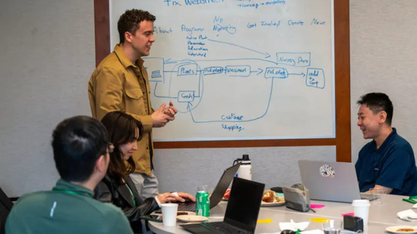 four hfid students sit around table and white board brainstorming