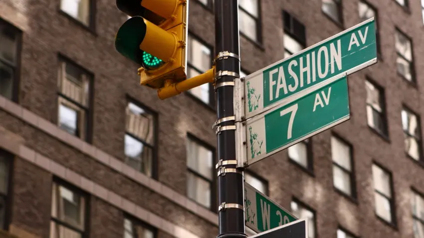 A stoplight in New York City with accompanying green street signs indicating Fashion Ave and 7th Ave.