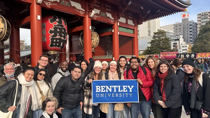 Group of people standing in front of a Japanese building holding a sign that says Bentley University