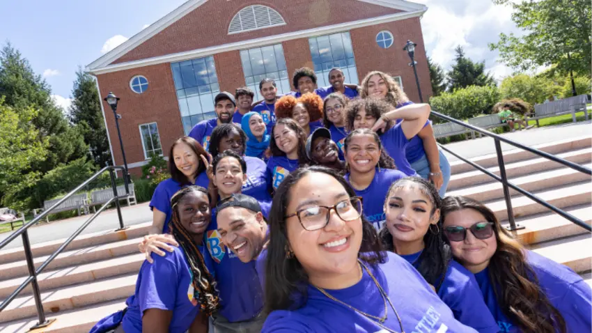 A group of ambassadors for the Bentley MOSAIC pre-orientation programs gather in front of steps on campus