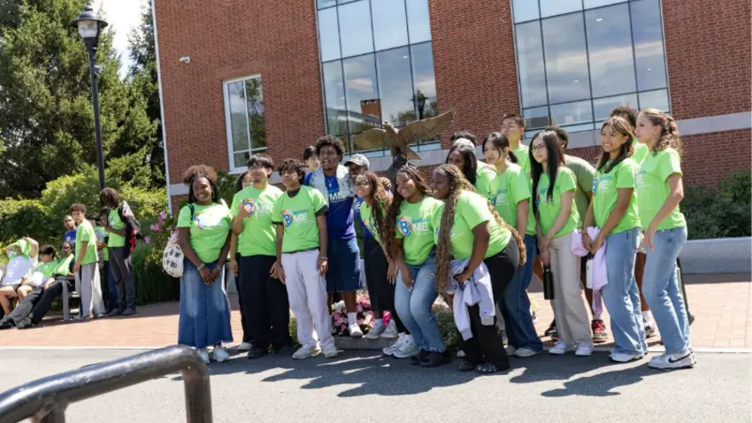 A group of first-year students at Bentley's MOSAIC pre-orientation program gathers in front of the falcon statue on campus