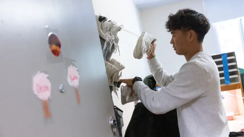 Bentley student adjusts sneakers on wall of dorm room as they unpack during Class of 2029 move-in day