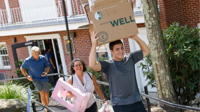 Bentley student carrying box on head with parent following behind during Class of 2029 move-in day