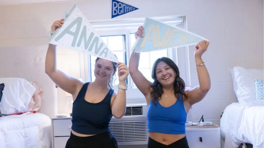Two Bentley roommates hold pennants with their names in their dorm room during Class of 2029 move-in day