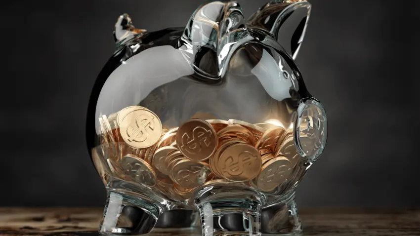 Photo of clear glass piggy bank filled halfway with gold coins.