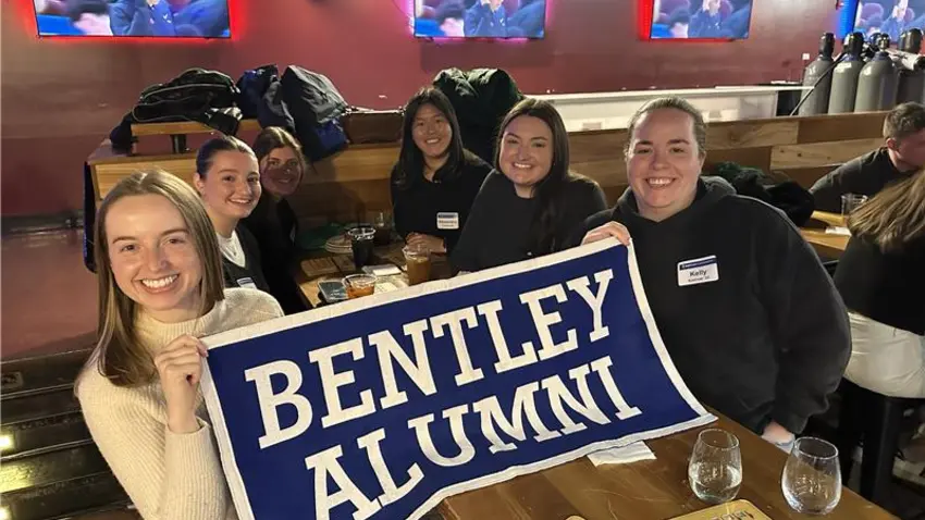 FOLD alumni smiling and holding a Bentley Alumni banner at FOLD Super Bingo