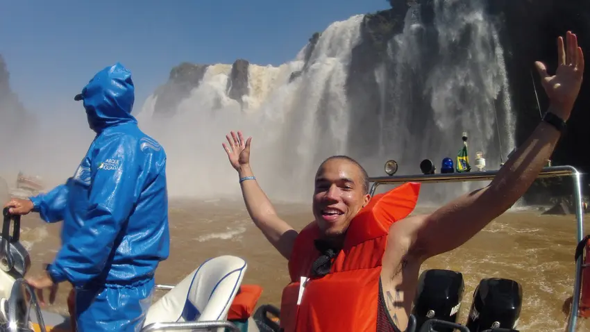 Student studying abroad. On a board by a waterfall. Looking very excited to be there with arms wide open.