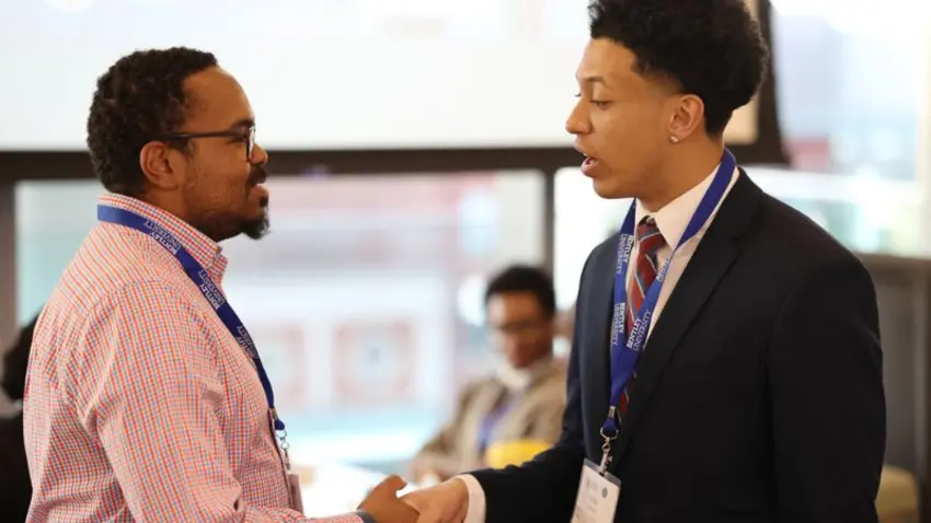 Bentley student shakes hands with an attendee at the Bentley Mankind Movement networking conference