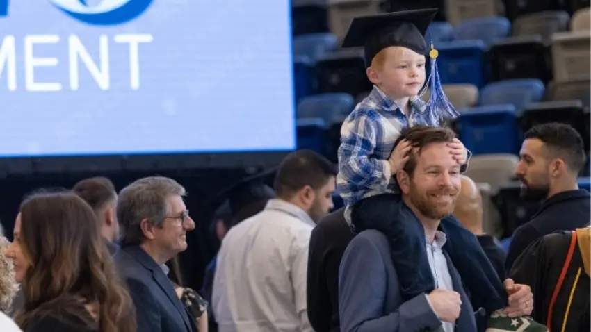 Toddler on the shoulders of an adult wears a family member's graduation cap at the end of the McCallum Graduate School of Business 51st commencement ceremony. 