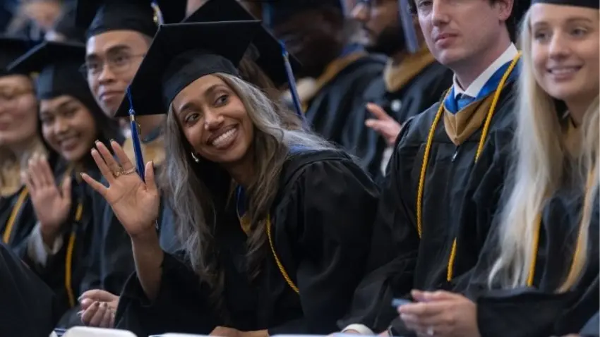 A graduate smiles and waves during the McCallum Graduate School of Business 51st commencement ceremony. 