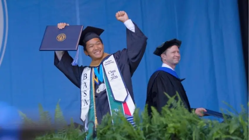 Bentley Class of 2026 graduate raises his diploma in the air as he crosses the stage