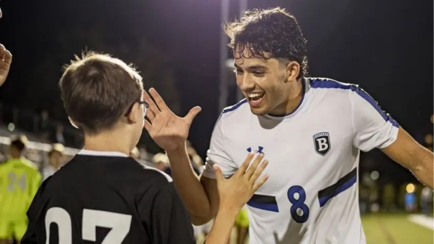 Bentley student and men's soccer player Michael Haikal high fives a youth on the soccer field