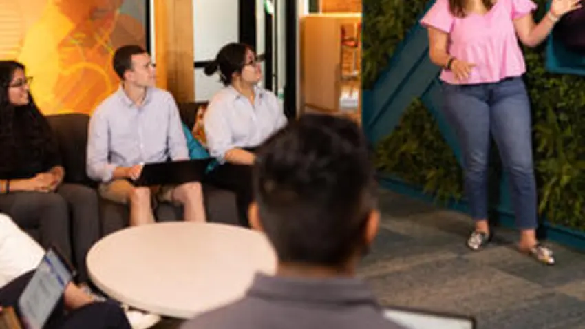 Woman stands at the front of a room, lecturing a graduate seminar