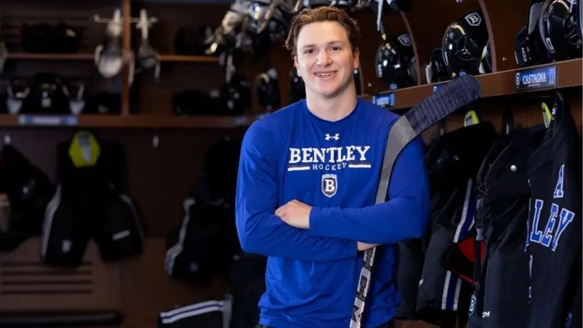 Bentley student Stephen Castagna leans against a hockey stick in the locker room for the men's hockey team