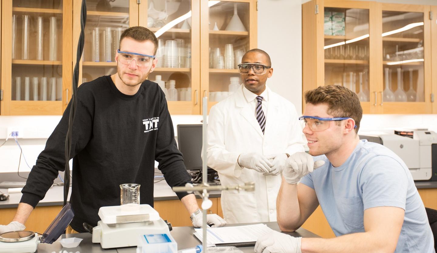 Professor conducting scientific lab experiments with two students.
