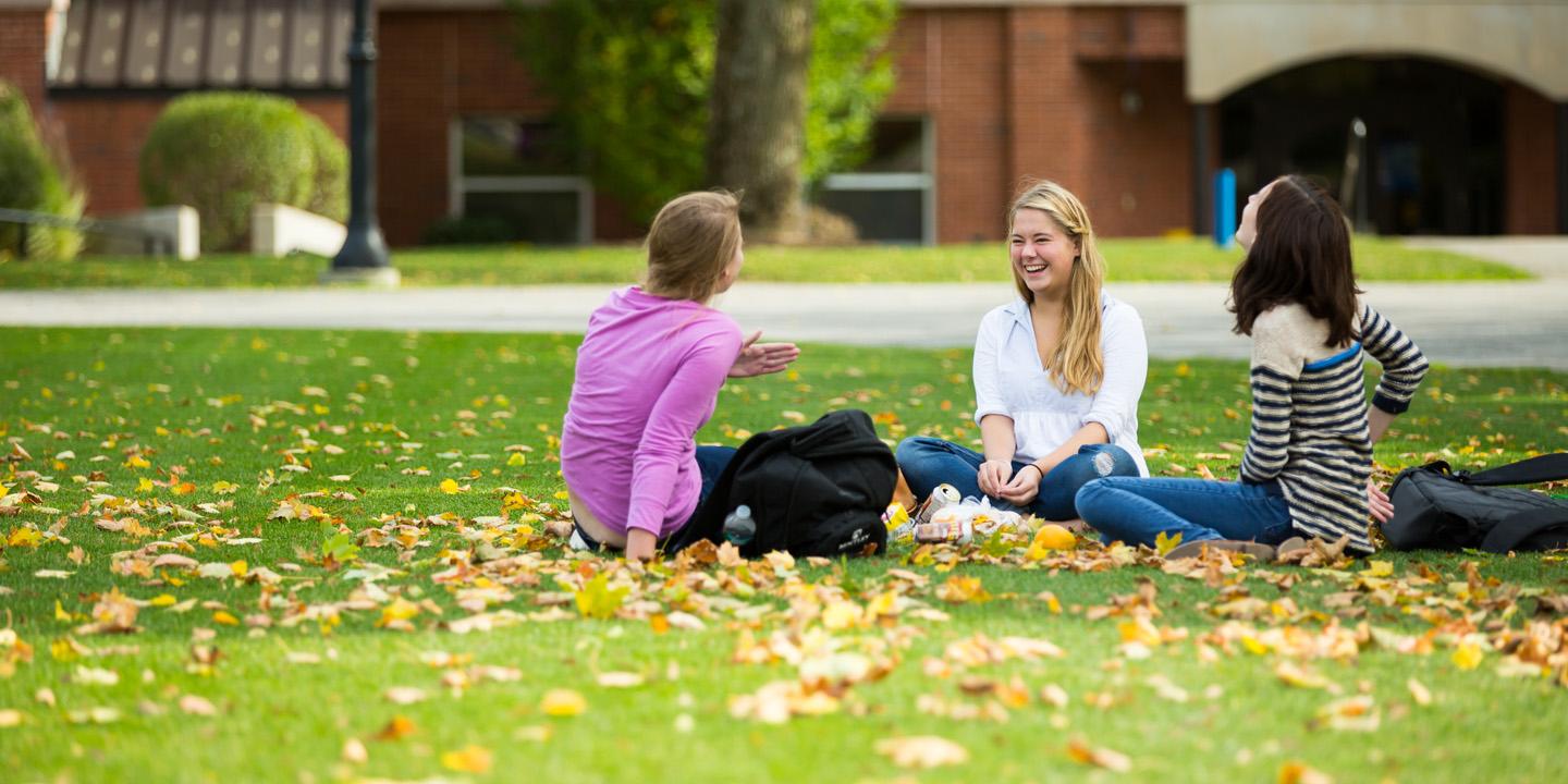 three students sit on the greenspace at bentley