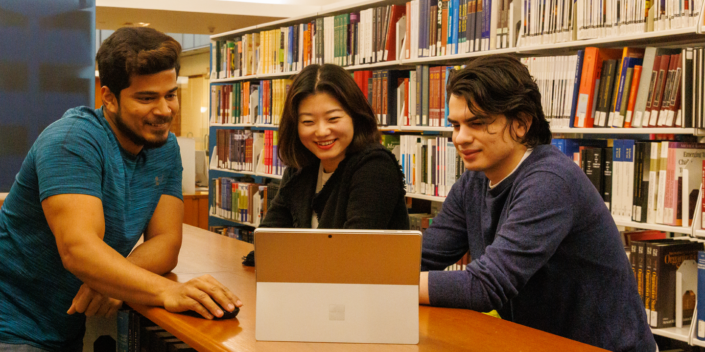three students work in library together and look at ipad 