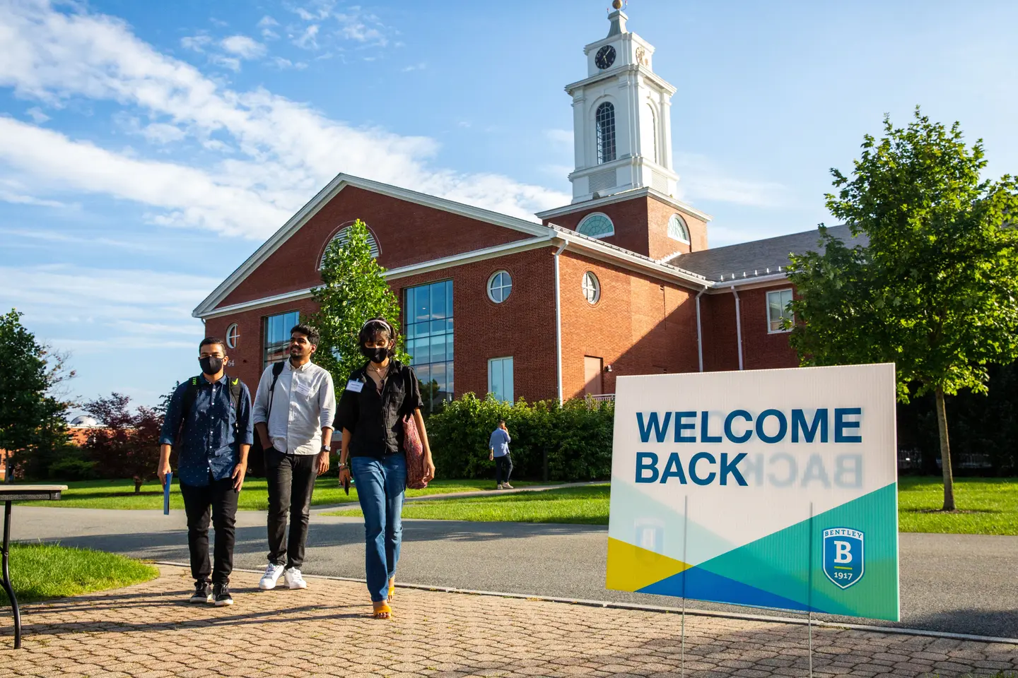 three students walking in front of library near sign reading Welcome Back