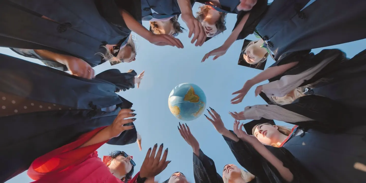 Graduating students in gowns reaching for a globe, ready to make a global impact and create positive change