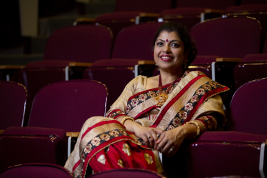Professor Mita Das, wearing a red and gold embroidered sari, sits in a seat in Wilder Auditorium.