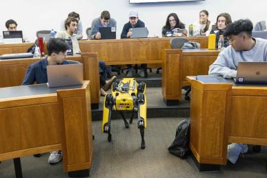 Students look at Spot the Robot, who is walking up a classroom aisle