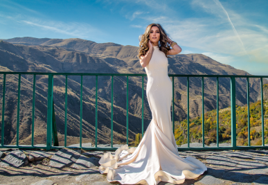 Kristina Ayanaian ’19 poses on a balcony overlooking the Caucasus Mountains in Armenia. She wears a sleeveless ivory evening gown with a flowing fishtail hem.