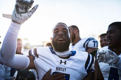 Jailen Branch In white Bentley football uniform with hand in the air