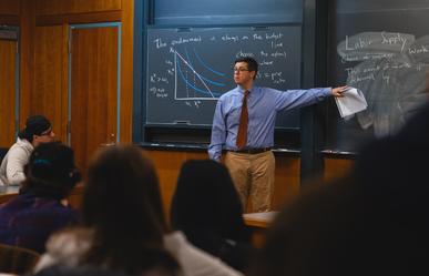 Assistant Professor of Economics Ben Chartock stands in front of a chalkboard in a classroom while teaching Bentley students.
