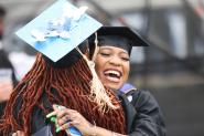 Graduates embrace at the 2022 Commencement ceremony. One woman's cap is adorned with blue butterflies and says "22" in beading across the top. 